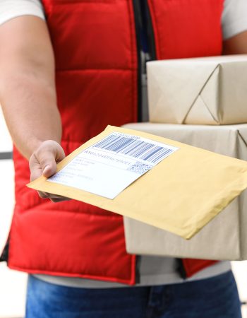 Young courier holding parcels on doorstep, closeup. Delivery service